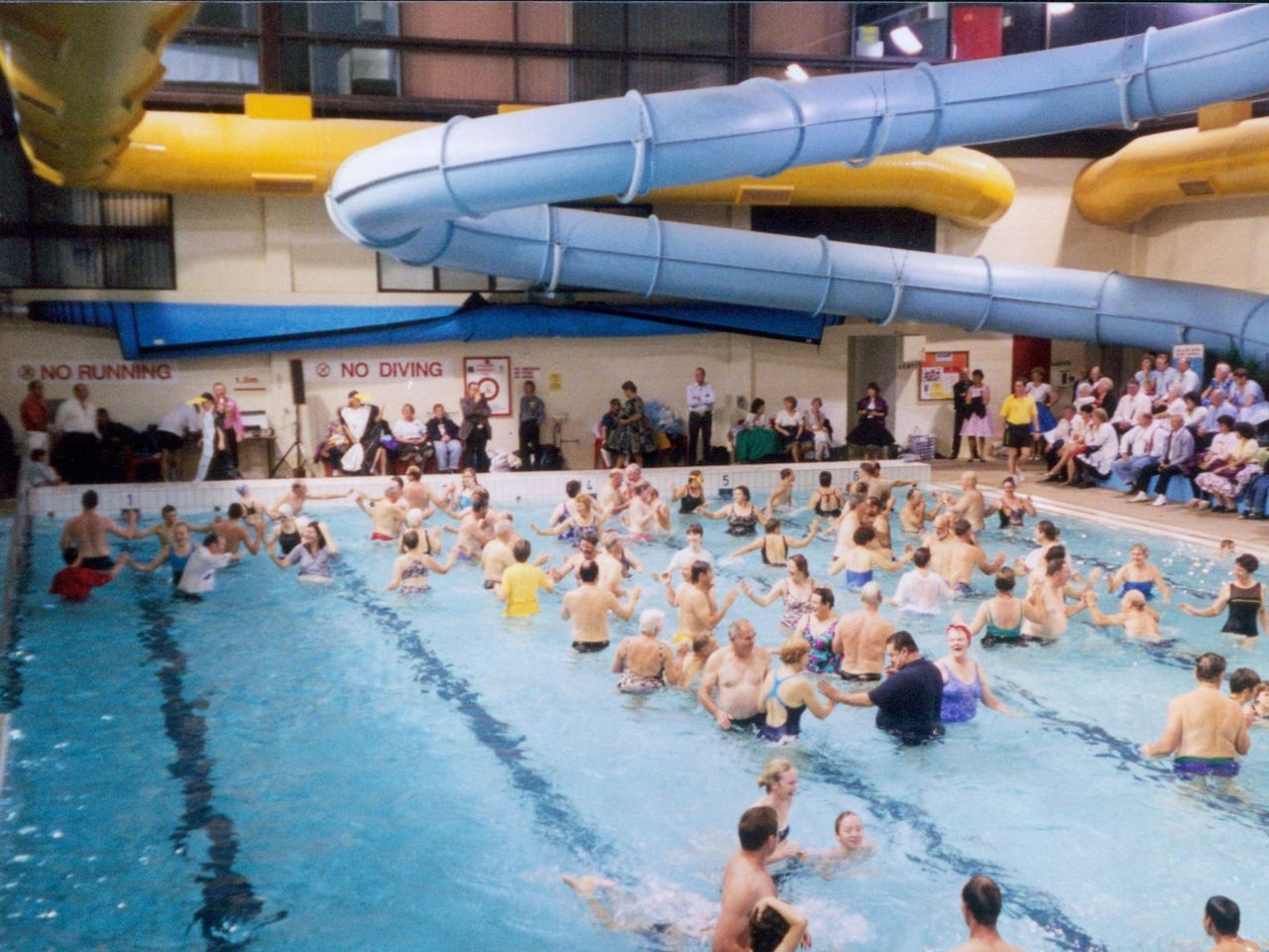 People in the swimming pool with the waterslide on the top of the picture