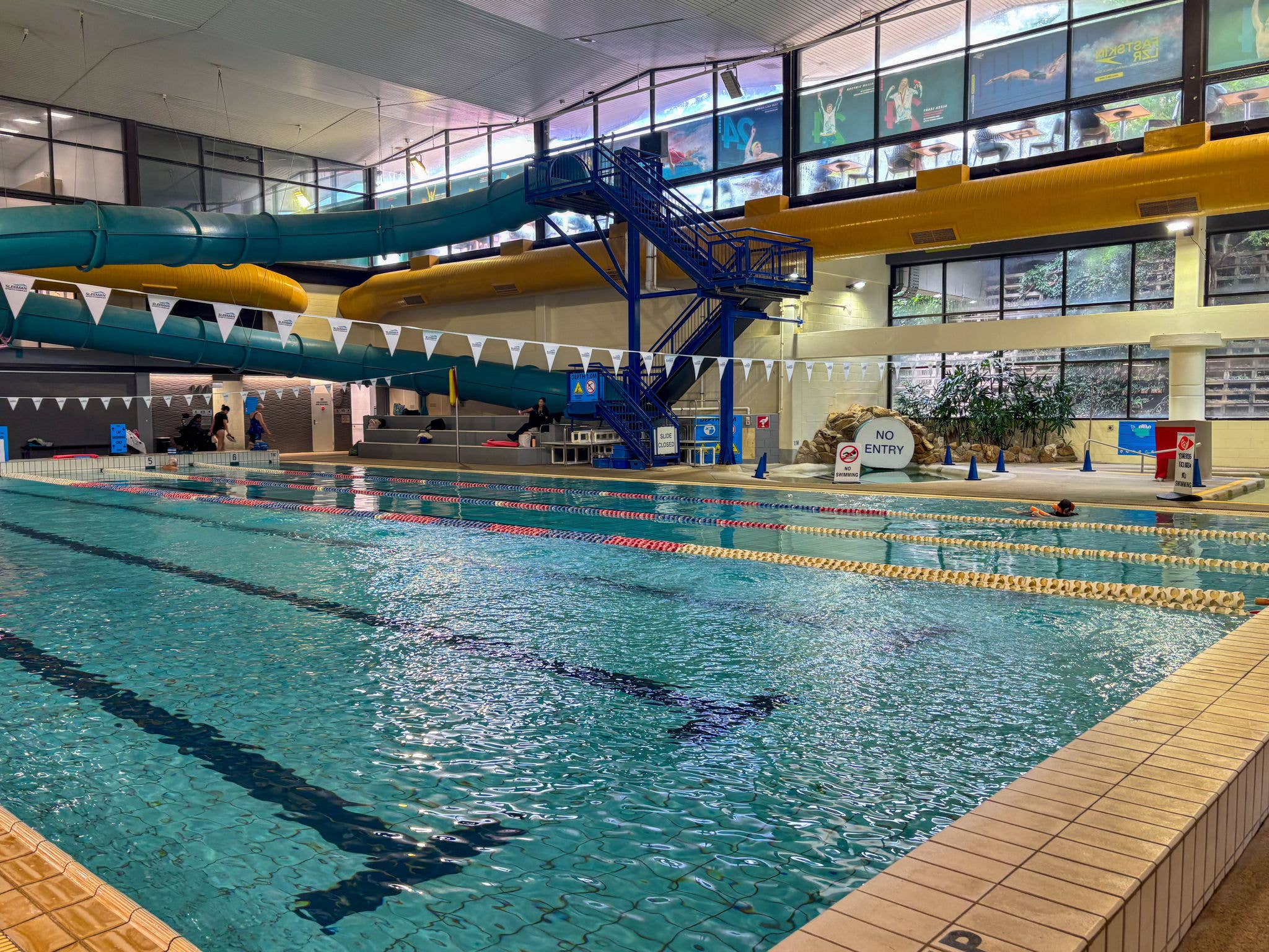 A pool with people in it and a colourful waterslide in the background