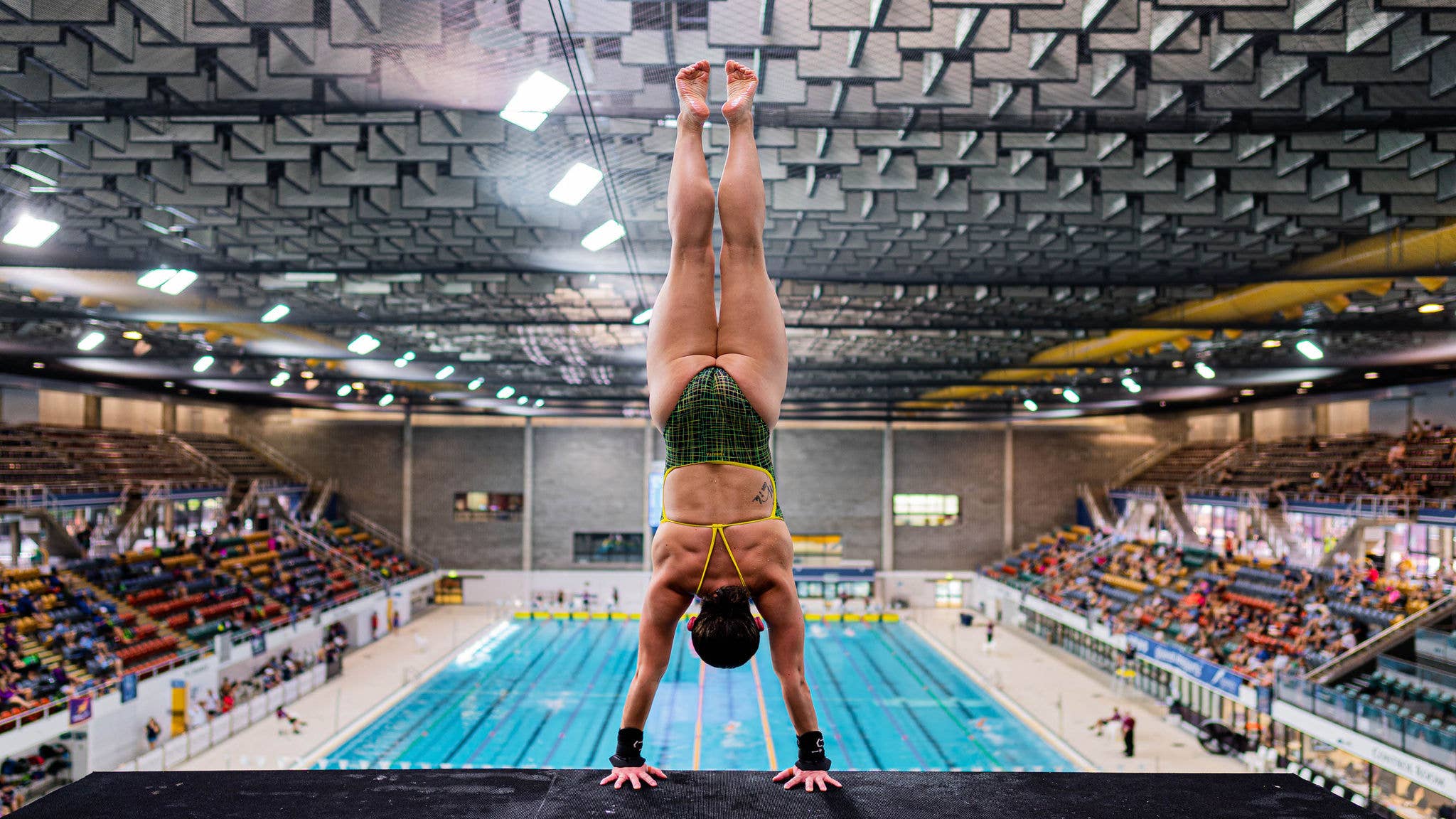 A female diver in a handstand prepares to dive as spectators watch