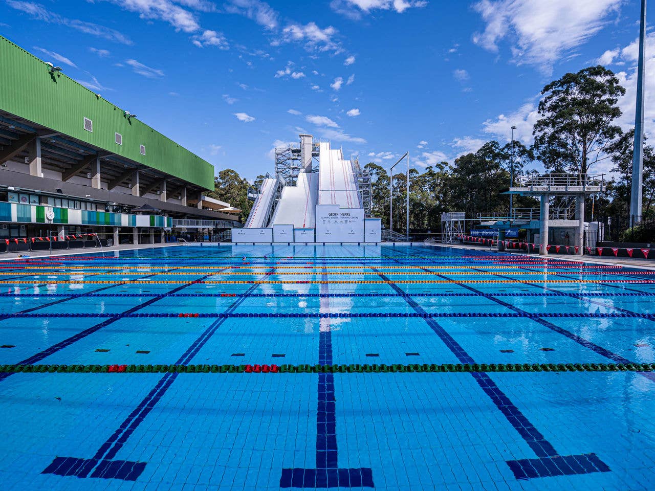 An outdoor 50m pool with lane markers and a ski jump in the background