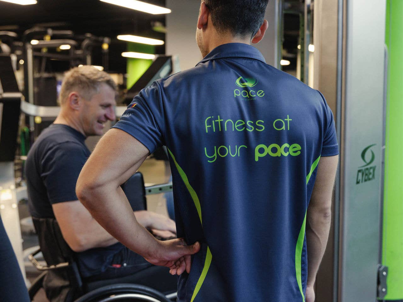 The back of a male on a bicycle wearing a shirt that says 'fitness at your pace'