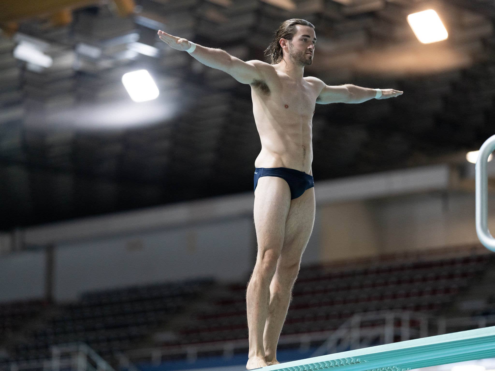 A male diver stands prepared to dive backwards off the high dive tower