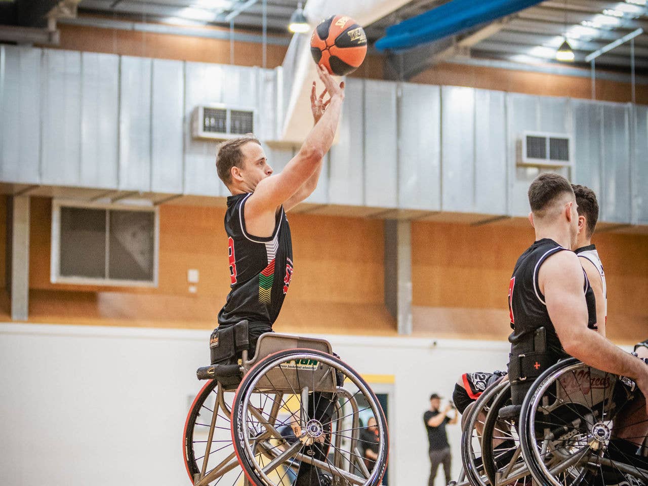 A basketballer in a wheelchair is reaching up to shoot